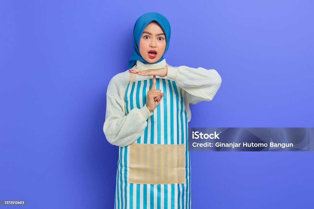 Portrait of shocked young housewife woman in hijab and apron showing time out gesture with hands isolated on purple background. People housewife muslim lifestyle concept 20-24 Years Stock Photo