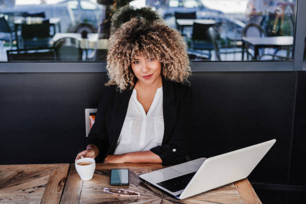 confident hispanic afro business woman in cafe working on laptop and mobile phone.business,lifestyle stock photo