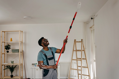 African-American professional painter paints the ceiling indoors
