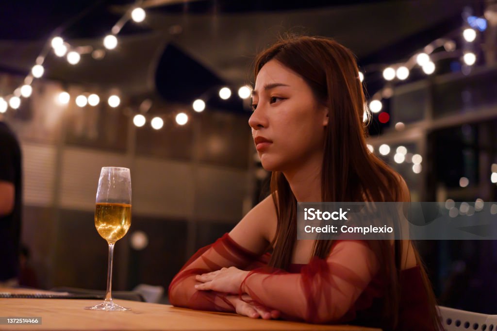 Young Asian woman feeling sad and heartbroken after breaking up with her boyfriend while sitting at restaurant Party - Social Event Stock Photo