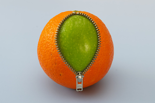 Image composition of an orange with a zipper, where a green apple comes to light