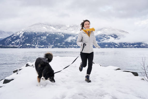 lächelnde frau läuft mit ihrem hund bei einem winterspaziergang am meer - snow dog walking running stock-fotos und bilder