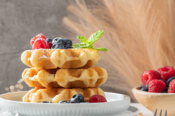 istock Traditional Belgian waffles stacked with fresh raspberries and blueberries sprinkled with powdered sugar on the kitchen counter 1372525680