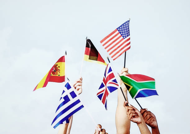 Group of hands hold variety of national flags aloft: US, German, British, South African, Spanish and Greek stock photo