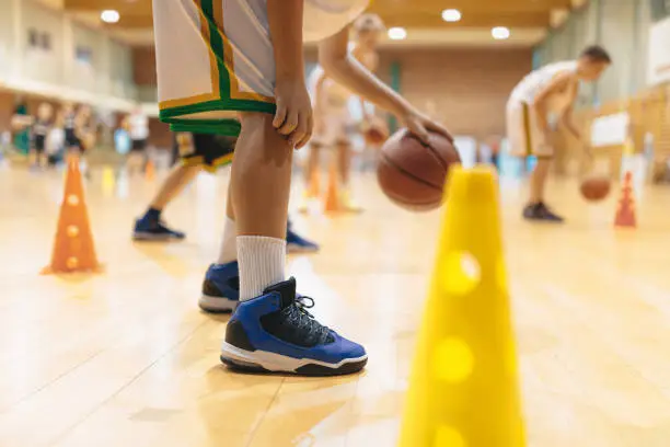 Photo of Young basketball players bounce balls on training session. School of basketball for kids. Children in basketall sport clothing improving skills