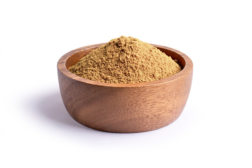 Ginger ground or dried brown plant powder in wooden bowl isolated on white background.