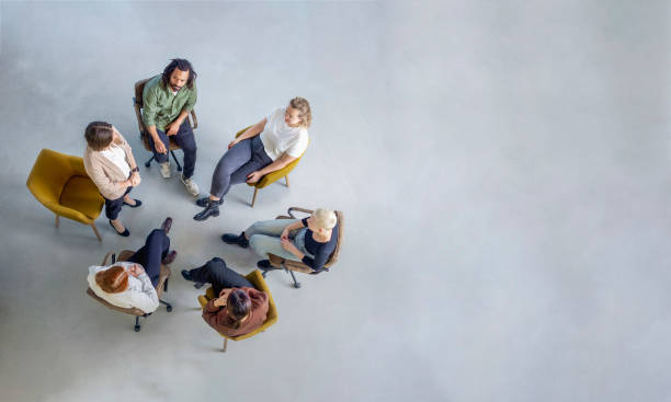 Woman sharing her experiences during a group therapy session Directly above shot of a group of people sitting in circle in support group session. Young woman sharing her experiences during a mental health group therapy meeting. group therapy stock pictures, royalty-free photos & images