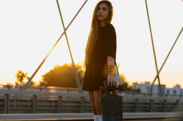 istock Young woman holding her longboard and standing on the bridge 1372540414