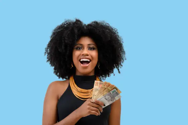 Photo of young black woman smiling holding brazilian money bills, positively surprised, space for text, person, advertising concept