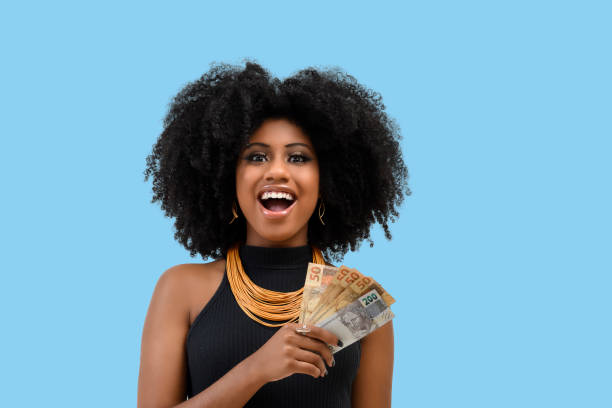 jovem mulher negra sorrindo segurando contas de dinheiro brasileiro, positivamente surpreso, espaço para texto, pessoa, conceito de publicidade - dinheiro real - fotografias e filmes do acervo