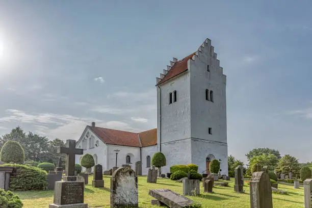 Photo of a white swedish church with a high tower, in the soft sunshine,