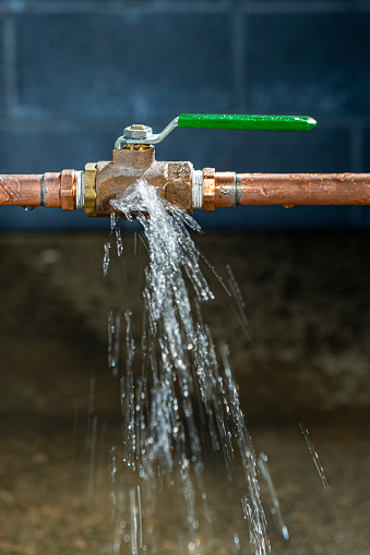 Looking down on a brass ball valve in a copper line, that has split from the frozen water inside, the valve has thawed out and is now spraying water onto the basement floor