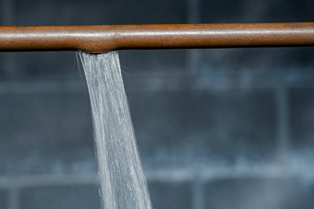A close-up of a ruptured copper pipe spraying water against a basement wall stock photo