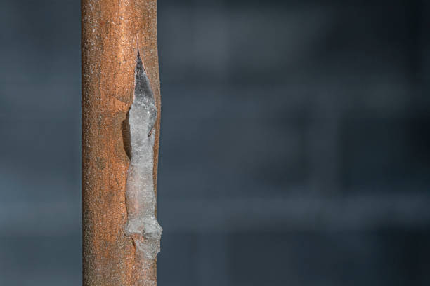 A close-up of a frozen copper pipe covered in frost against a basement wall stock photo