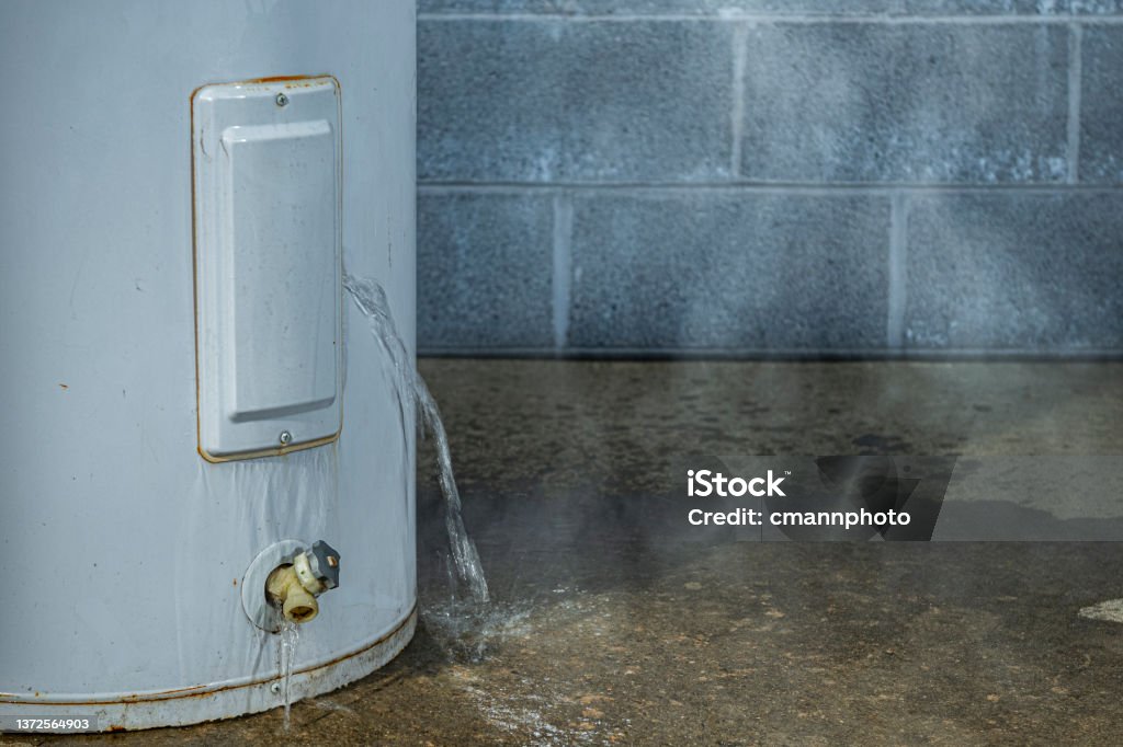 A close-up of a water heater leaking water on to the basement floor A close-up of water leaking out of an access panel of an electric water heater onto the concrete floor of a basement with a cinder block wall in the background. Boiler Stock Photo