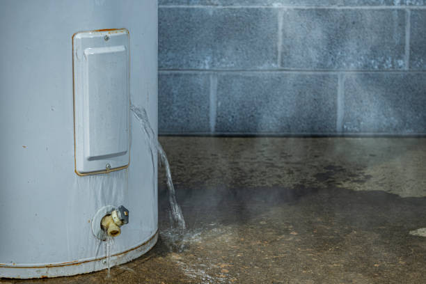A close-up of a water heater leaking water on to the basement floor stock photo