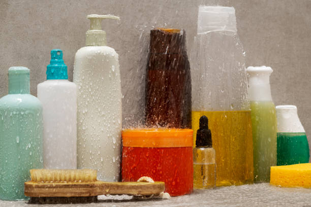 primo piano dei prodotti cosmetici sotto la doccia con spruzzi d'acqua su ceramica grigia - water splashing spray drop foto e immagini stock