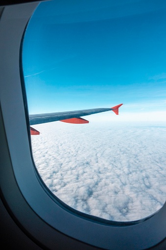 A wide shot, out of an airplane window of an airplane flying over clouds on a sunny day.