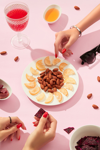 Dried fruits and nuts with sauce on pink background with womans hands. Healthy snacks food concept