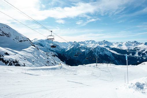 A wide shot of a ski lift carrying skiers to the top of the ski slopes in the French Alps on a sunny day.