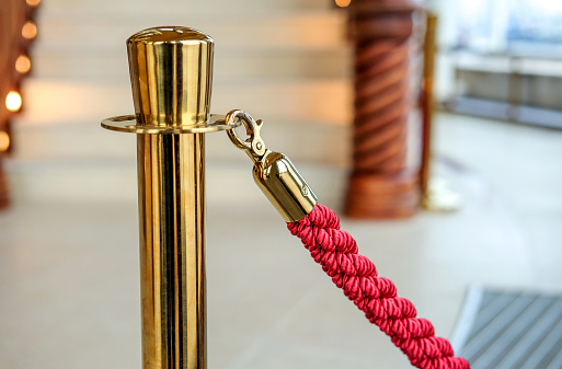 Gold-colored barrier with red cord in a luxurious foyer - close-up with selective focus and blurred background