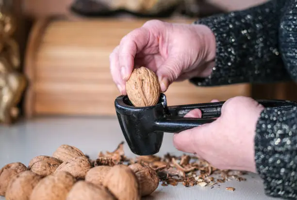 Elderly woman cracks walnuts with a nutcracker - selective focus, side view close-up