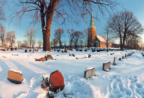 Winter landscape with a norwegian countryside church at sunset, graveyard on foreground