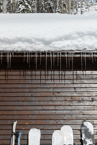 Wooden cabin with snowy roof and icicles and ski equipment equipment leaning against the wall