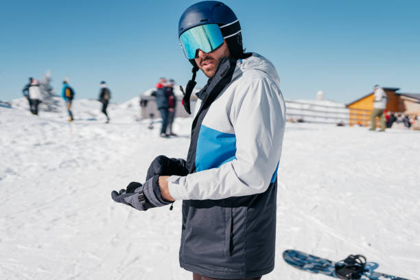 A young man, ready for action with skis and helmet, smiles broadly at the camera, embodying the happiness and positive emotion of engaging in his favorite hobby at a renowned ski resort