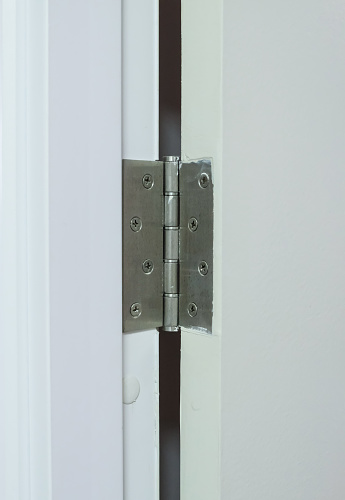 Closeup of the metal hinges on the white PVC door of the restroom in the urban house, front view for the copy space.