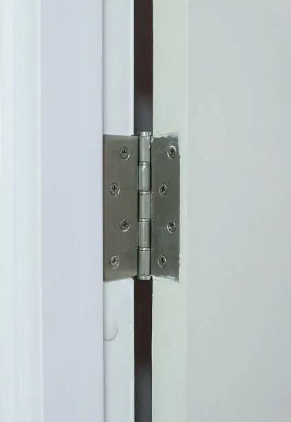 Closeup of the metal hinges on the white PVC door of the restroom in the urban house, front view for the copy space.