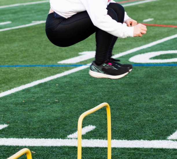 Girl jumping over plastic yellow hurdle on a turf field High school track and field runner jumping over a plastic yellow hurdle on a turf field. crossfit girl stock pictures, royalty-free photos & images