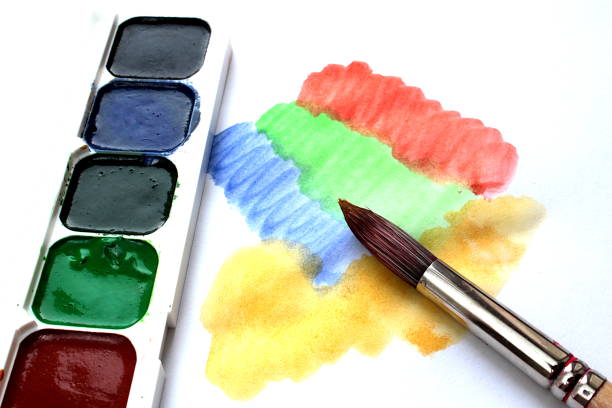 Watercolor paints and a brush for drawing are on a white sheet
