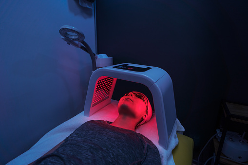 A young latin woman doing a red light therapy on her face.