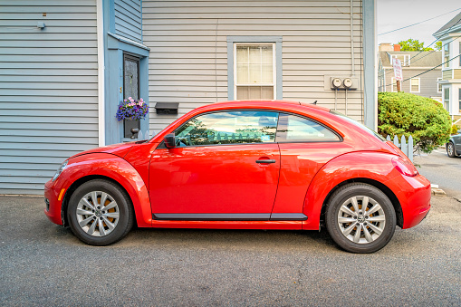 A red Volkswagen New Beetle is parked on a driveway in Salem, Massachusetts, USA on a cloudy day.