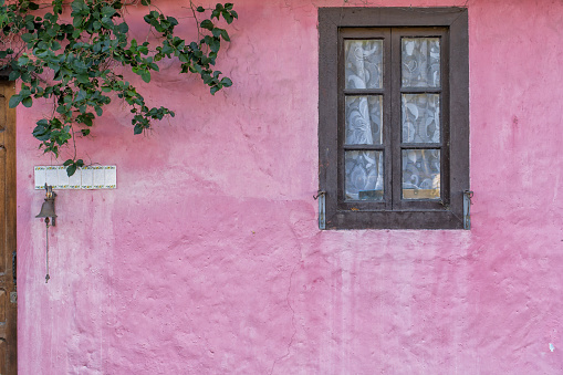 The facade of an old house painted pink with a window and a branch of bougainvillea