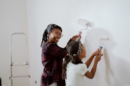 Mamá ocupada pasa tiempo con una hija alegre, la contrata para ayudarla, juntos pintan las paredes del apartamento en renovación, aplican pintura blanca con rodillos. photo