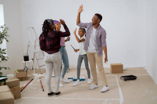 el equipo de la familia trabaja en conjunto durante la renovación del apartamento, los niños de cinco años con sus padres después de pintar con éxito las paredes alrededor del desorden de pinceles, rodillos de pintura cajas de escaleras - home improvement couple painting real estate fotografías e imágenes de stock