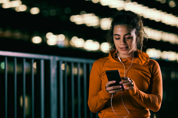 A happy female night runner is using the phone for music on a city street. stock photo