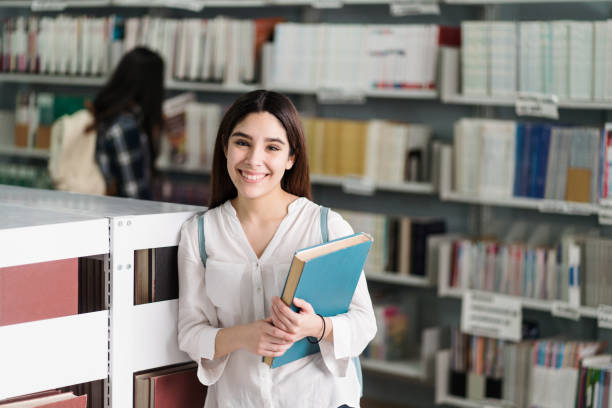 istock Happy student holding book and smiling at camera 1372604734