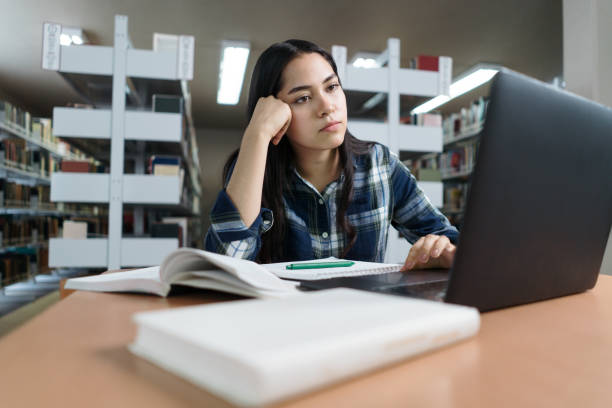 Bored female student doing homework in library stock photo