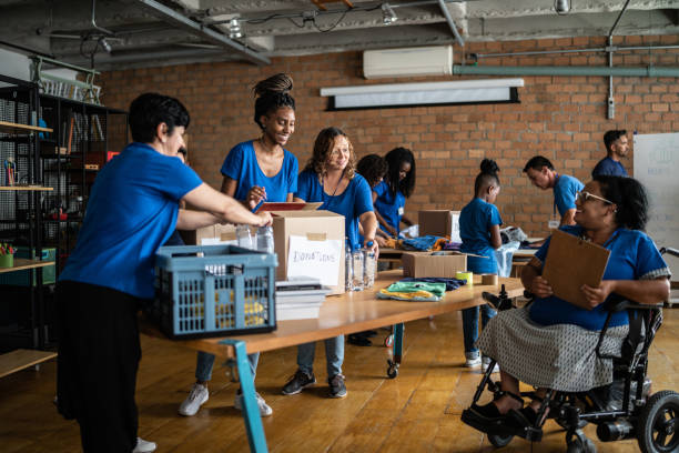 Volunteers arranging donations in a community center - including a disabled person Volunteers arranging donations in a community center - including a disabled person non profit organization stock pictures, royalty-free photos & images