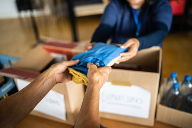 la mano del volontario che fa donazioni a una persona in un centro comunitario - beneficenza foto e immagini stock