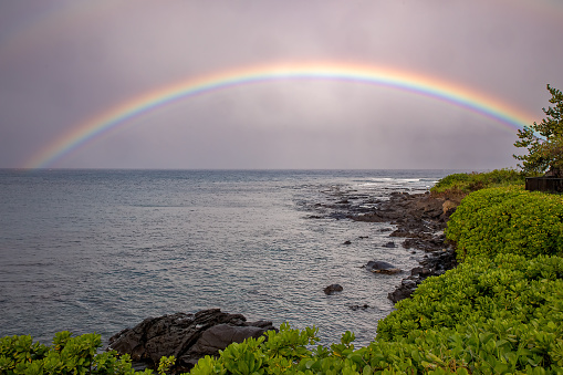 A rainbow in Maui over the rocky beach and ocean.