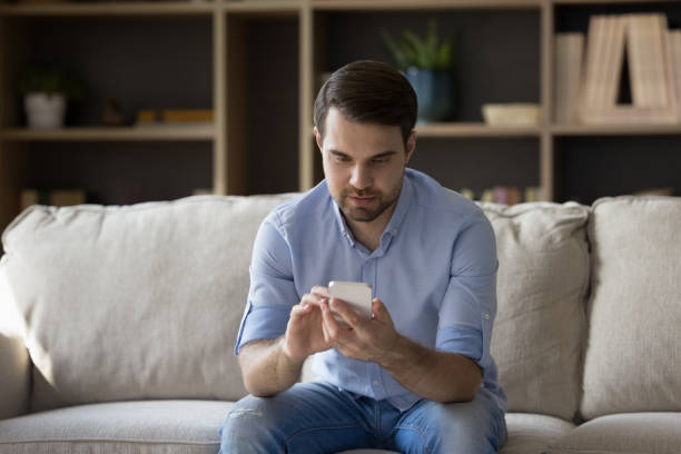 istock Focused millennial guy un casual using cellphone on couch 1372613198