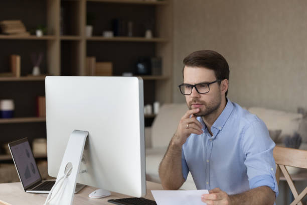 istock Focused millennial businessman wearing glasses thinking over project at workplace 1372613486