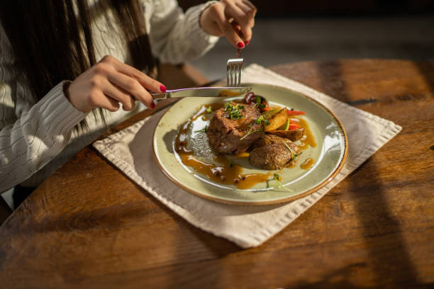Woman using fork and a knife for cutting tasty meat, she is on lunch alone in modern restaurant.