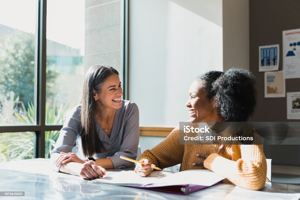 Caring female high school teacher tutors female student A female teacher tutors a teenage girl after school. They are smiling as they look at each other. Role Model Stock Photo