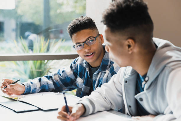 Male high school friends studying together A teenage boy talks to his friend as they study for a test together. serious black teen stock pictures, royalty-free photos & images