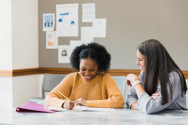 Math teacher helps female student A cheerful female teacher smiles as she helps a female high school student with a math problem. The teacher smiles as she understands a math concept. high school high school student science multi ethnic group stock pictures, royalty-free photos & images